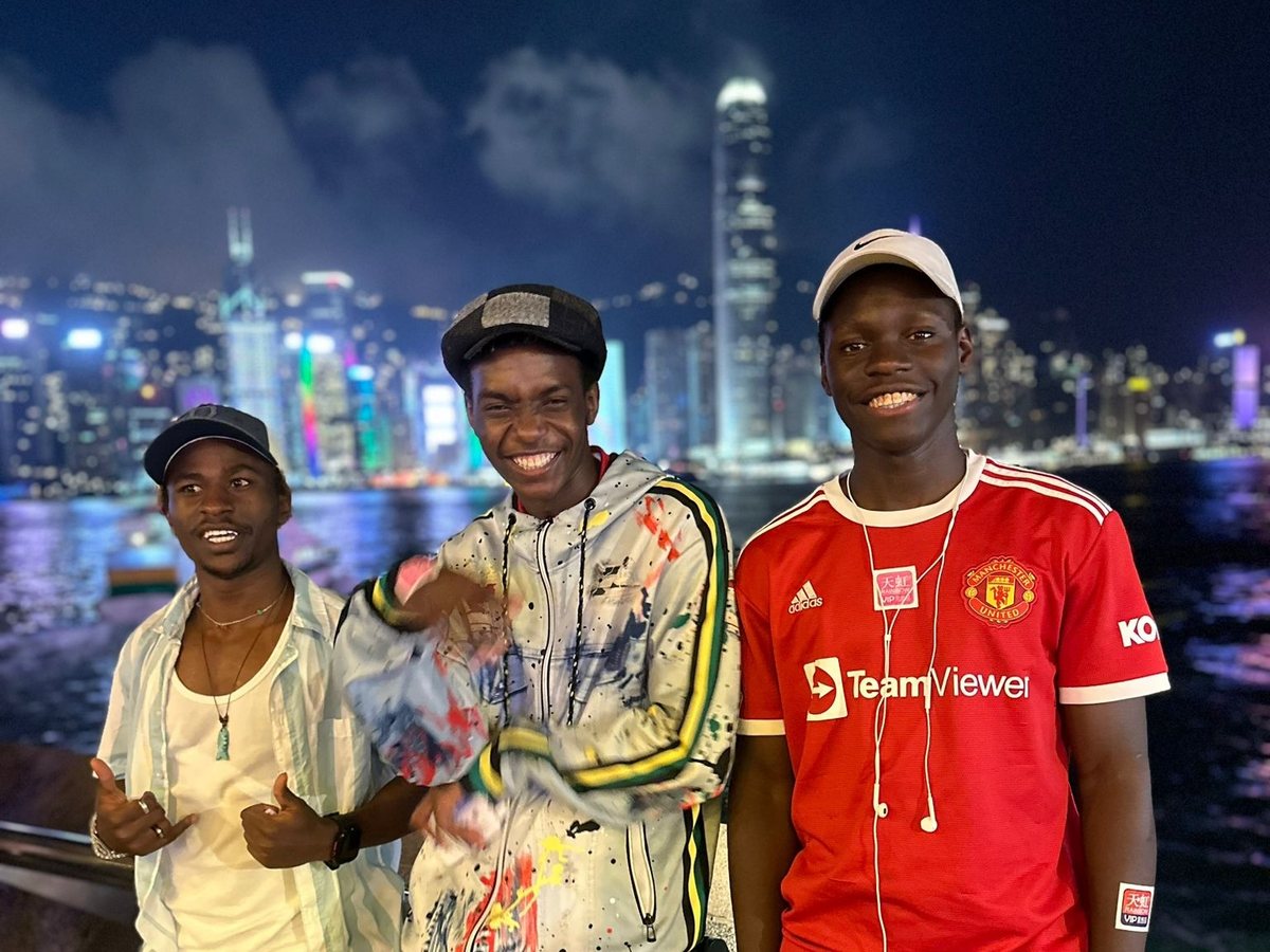 Three Exchange participants smiling against the Hong Kong harbour skyline at night